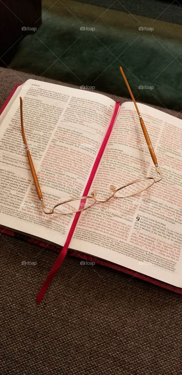 Reading glasses lying on a bible open to the book of John, lying on a pew in a church with the bookmark laid through the page.