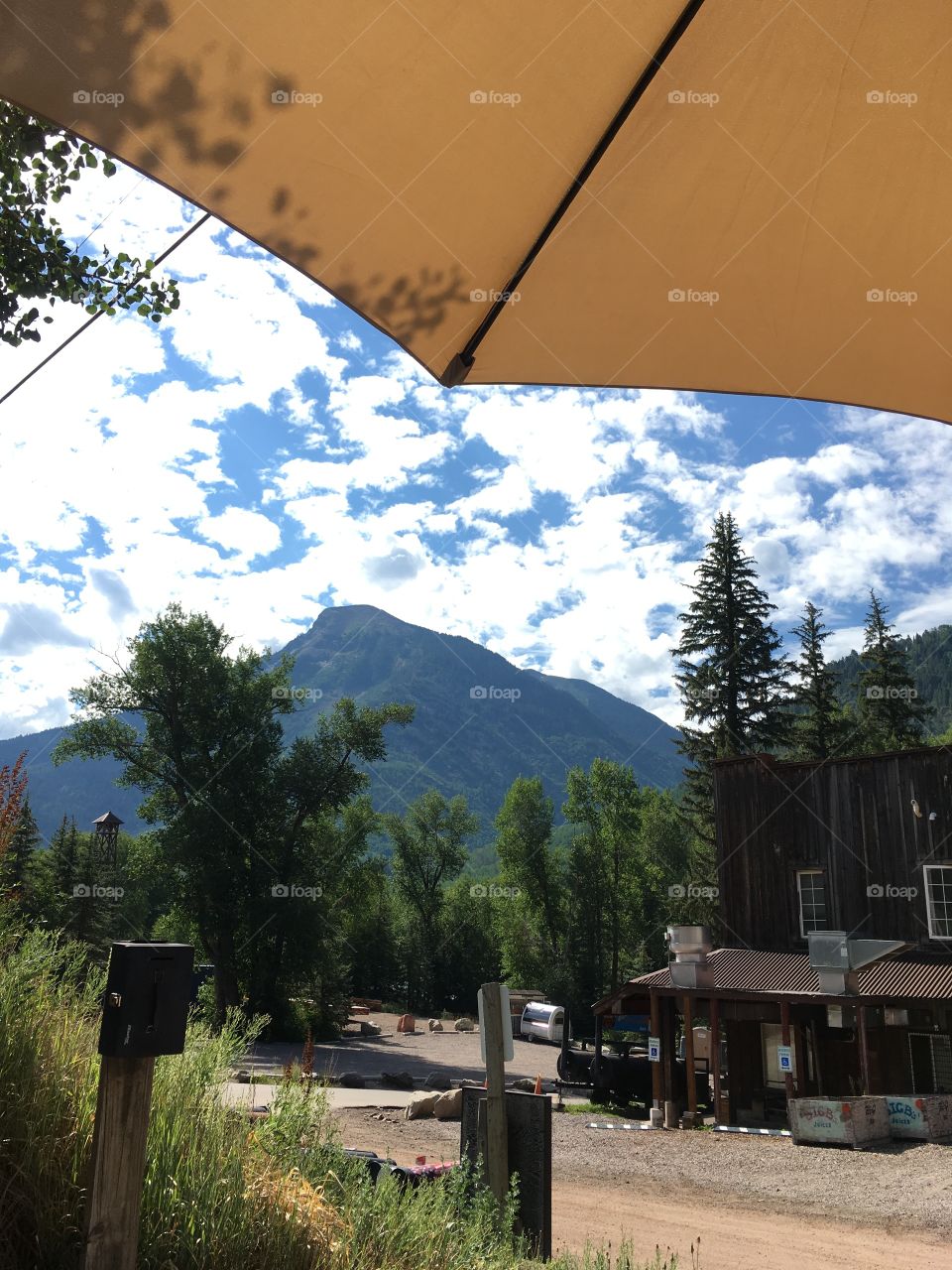 Viewing a beautiful mountain, blue sky’s & puffy white clouds while sitting under a cafe umbrella outside a small mountain town coffee shop. 