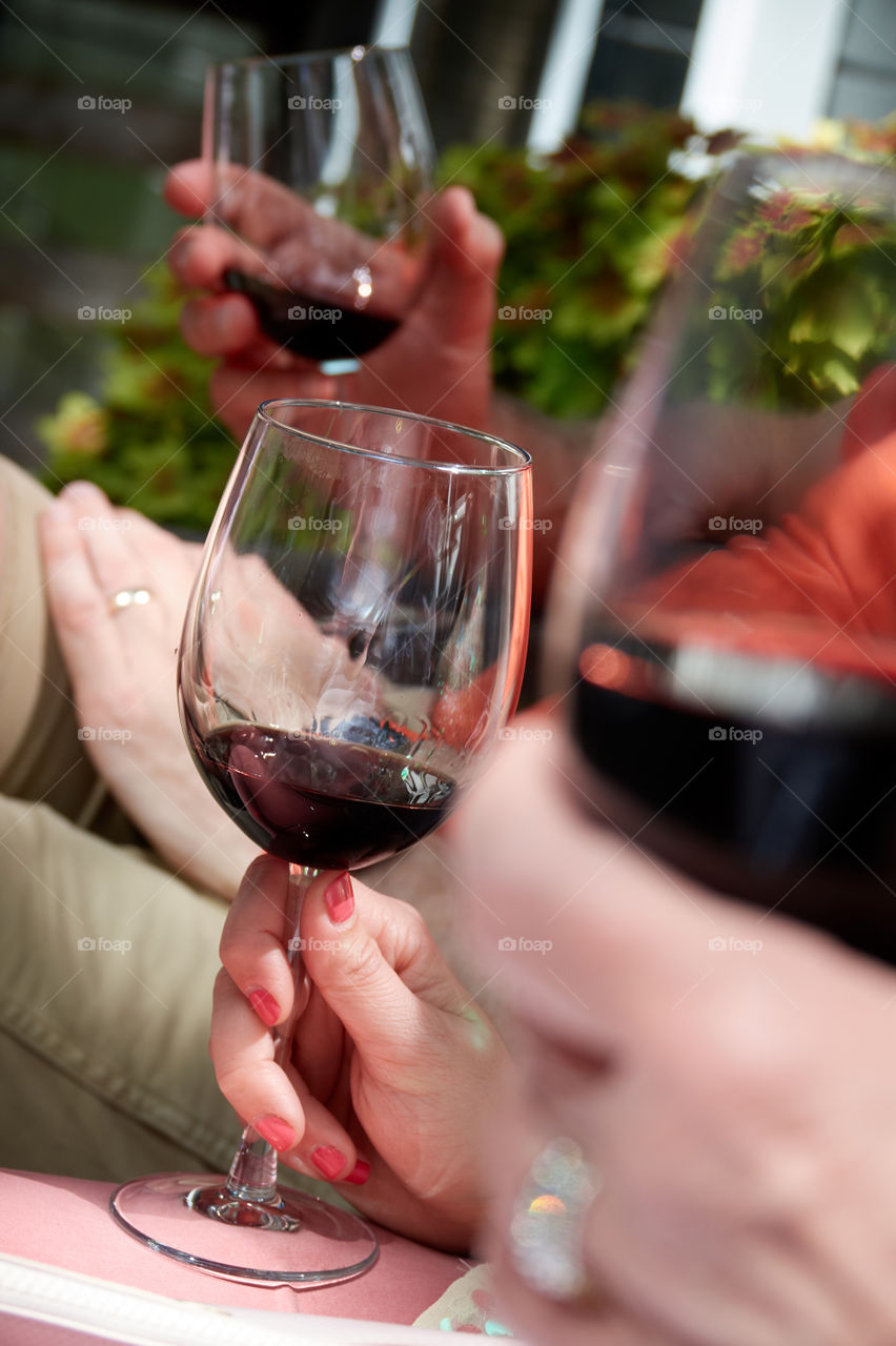 Closeup shot of people drinking red wine outside. One hand and glass are in sharp relief against a blurry background and foreground.