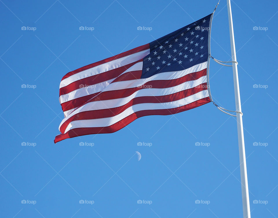 Flag blowing in the wind with moon during the day