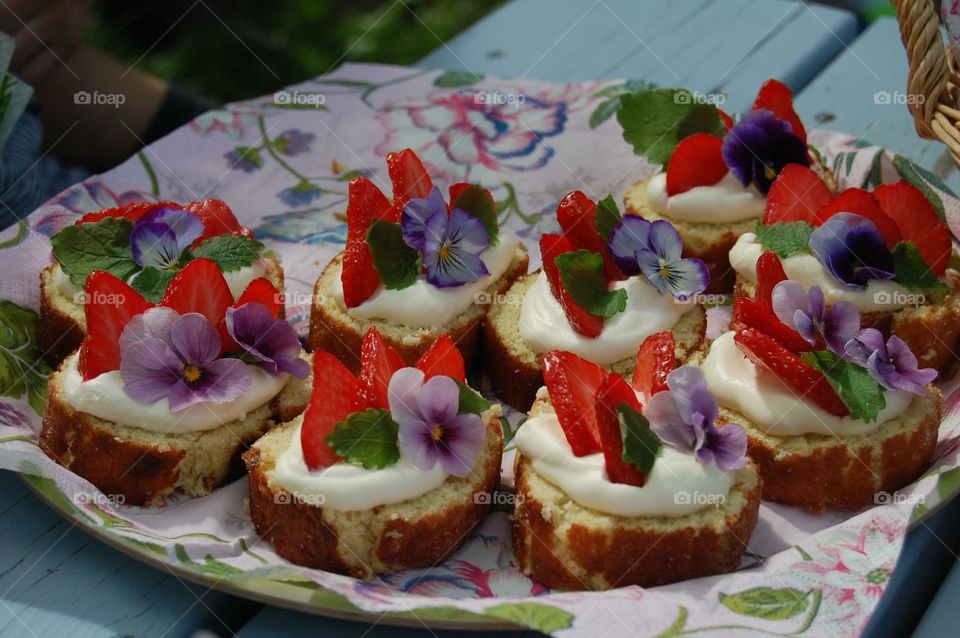 Pastry decorated with flowers and strawberries on tray outdoors
