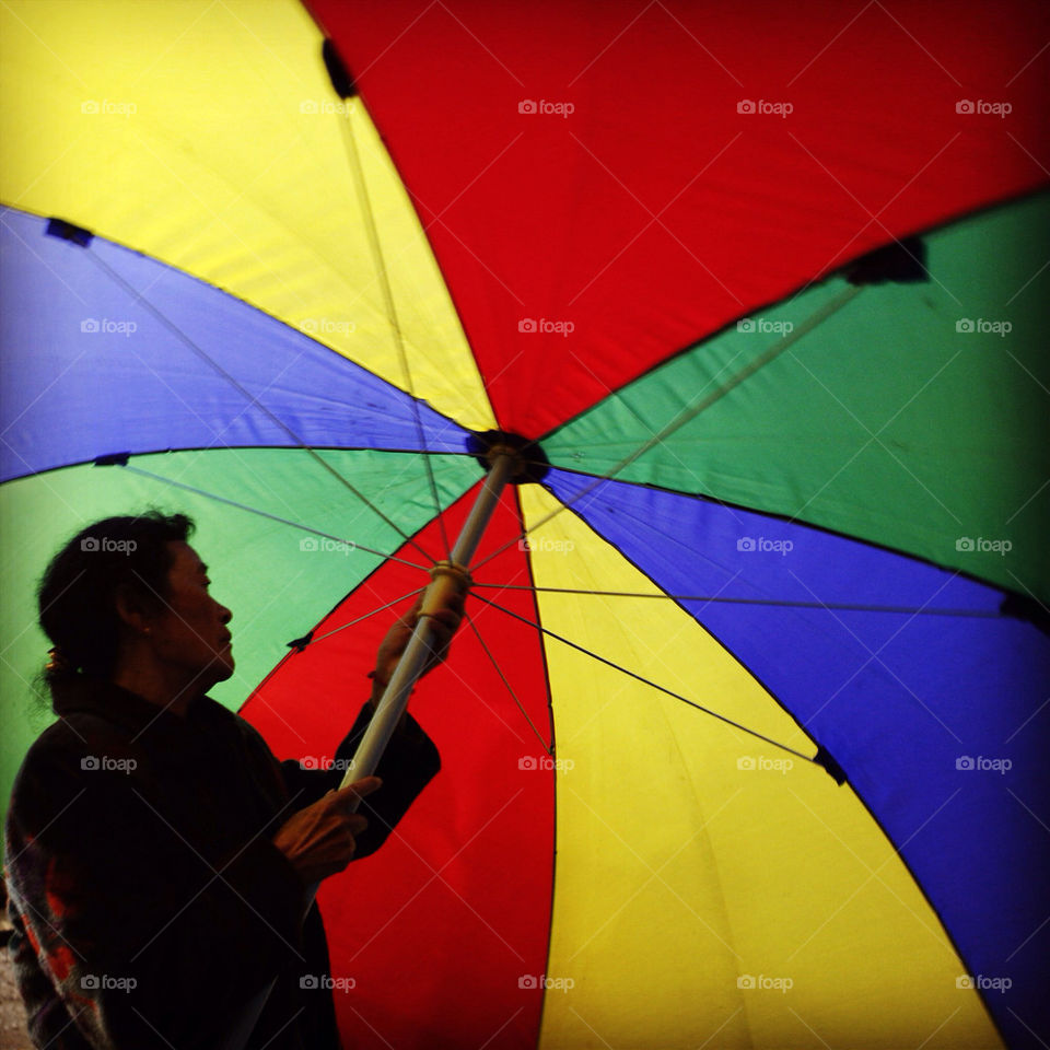 Asian adult opens large colorful umbrella with slight motion blur
