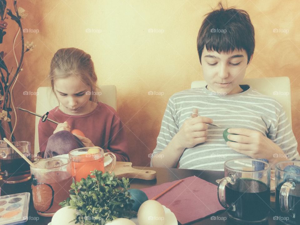 Brother and sister painting Easter eggs at home