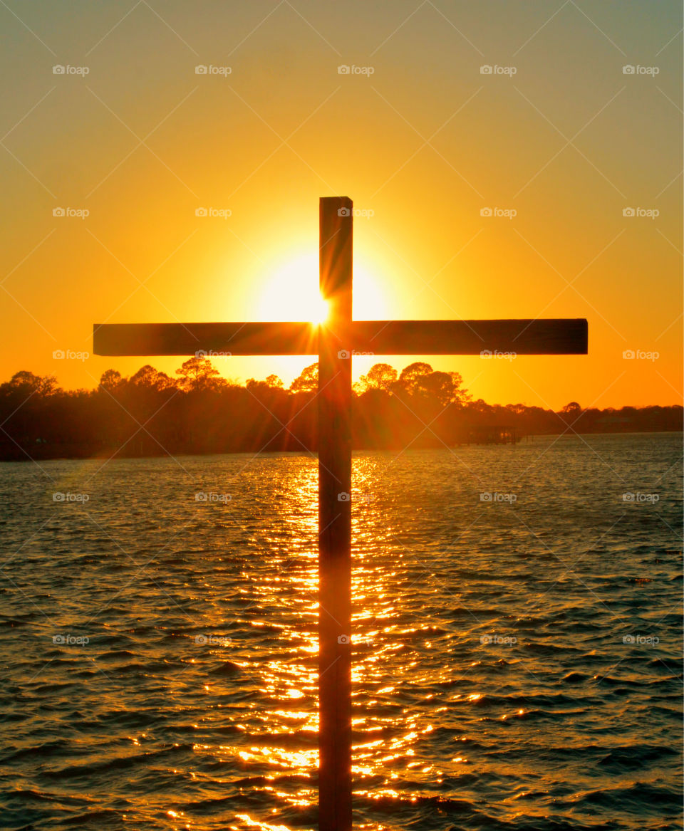 Silhouette of cross against lake at sunset