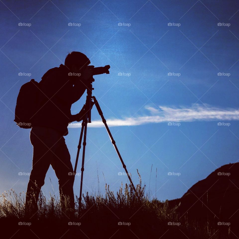 Silhouette of man taking a photo using a DSLR camera and a tripod. Image taken on a ridge in the Alberta Badlands.