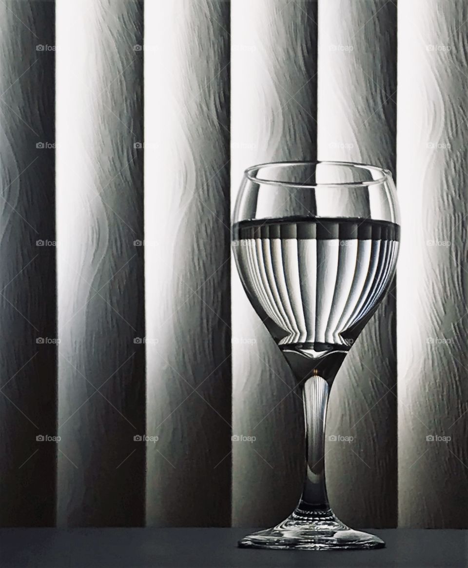 Natural lighting coming through the window blinds and reflecting in a wine glass 