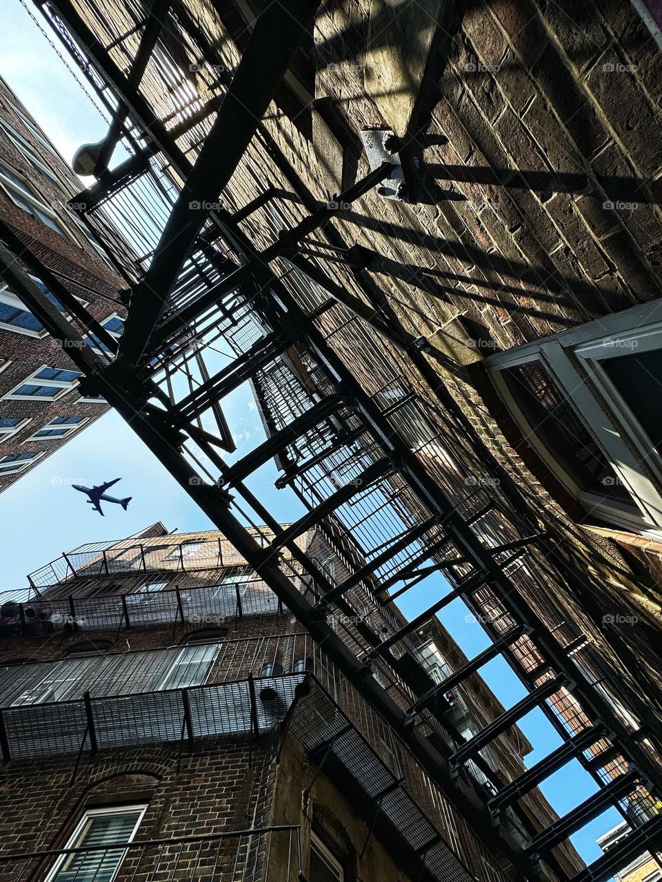 Looking up at an airplane through fire escapes in a narrow alleyway 