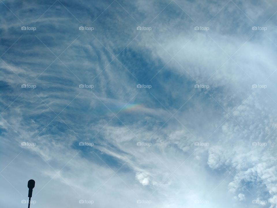 clouds in sky with tiny rainbow in center dalight.