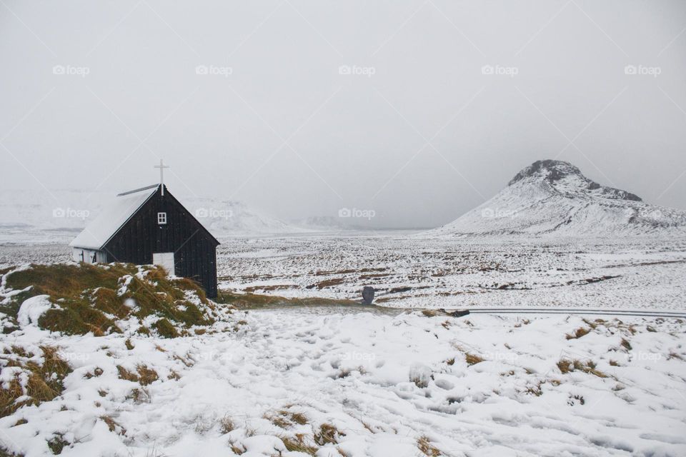 Snowy landscape in Iceland with snow-covered mountain and black church.