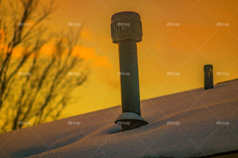 vent in the early morning sunrise on a snow covered rooftop