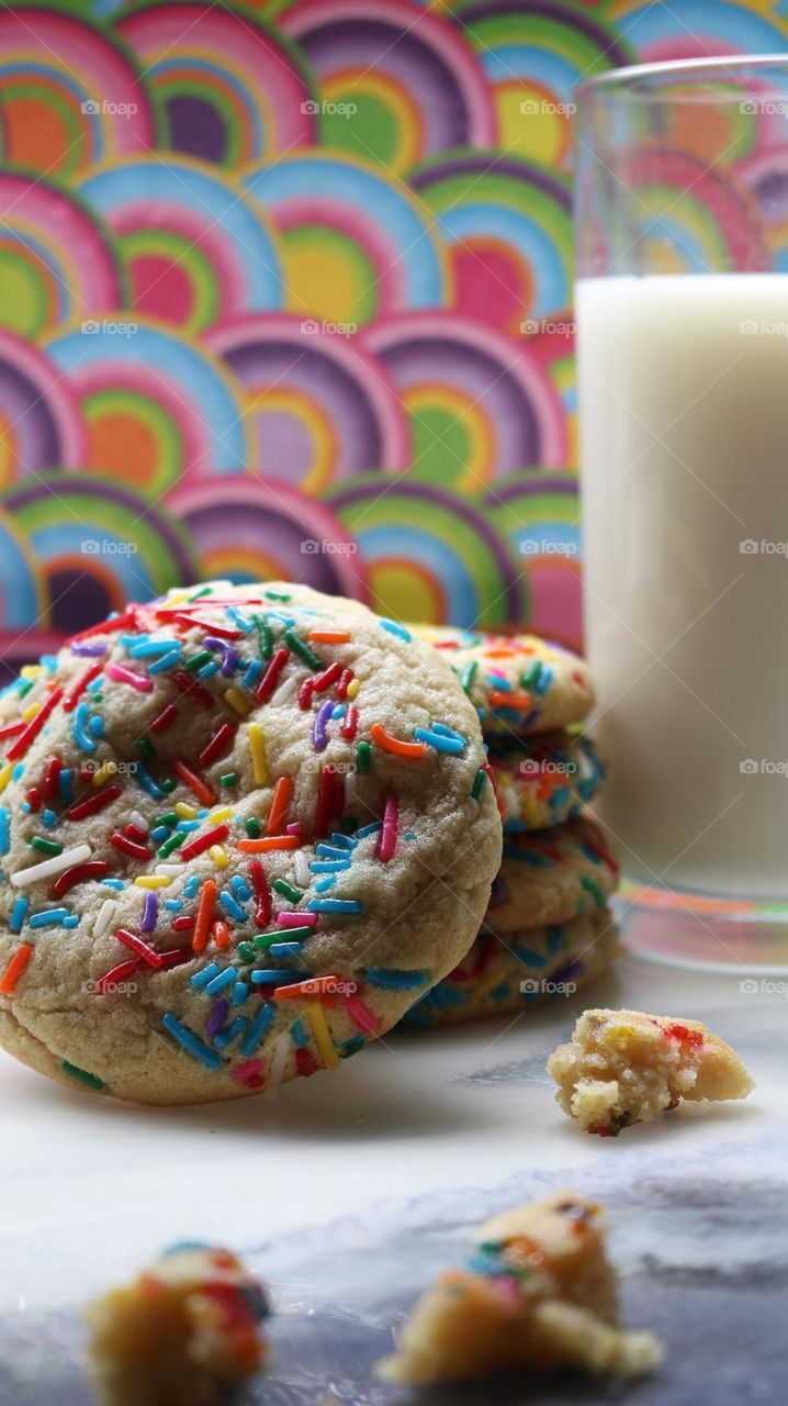 Rainbow sugar cookies alongside a glass of milk.