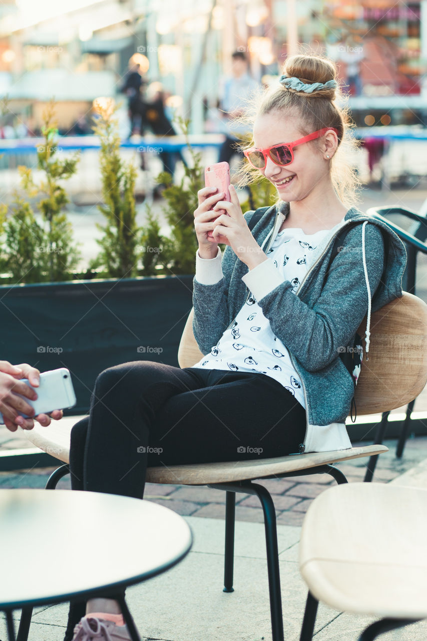 Teenage girl having fun using smartphone sitting in center of town