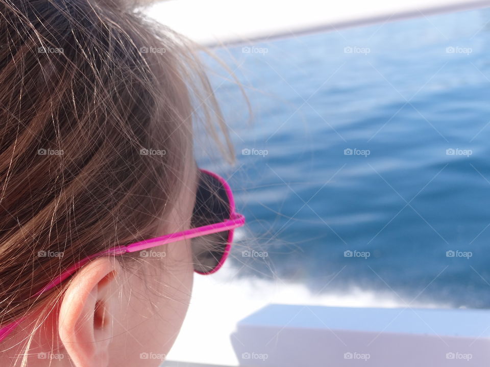 Looking Out Over the Water. Girl in pink aviator sunglasses, head turned away,looking out over large body of water