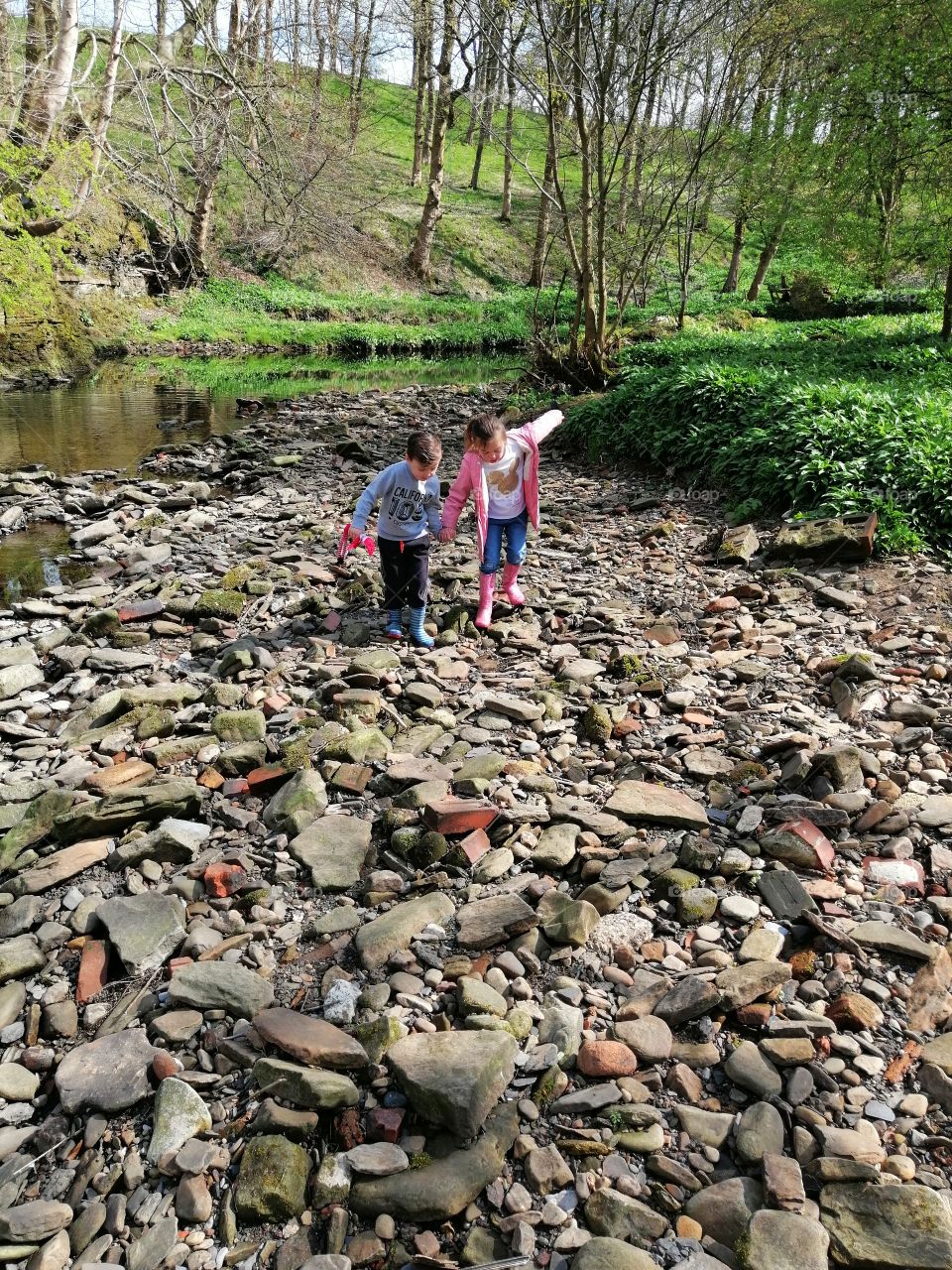 Kids helping each other over the rocky riverside