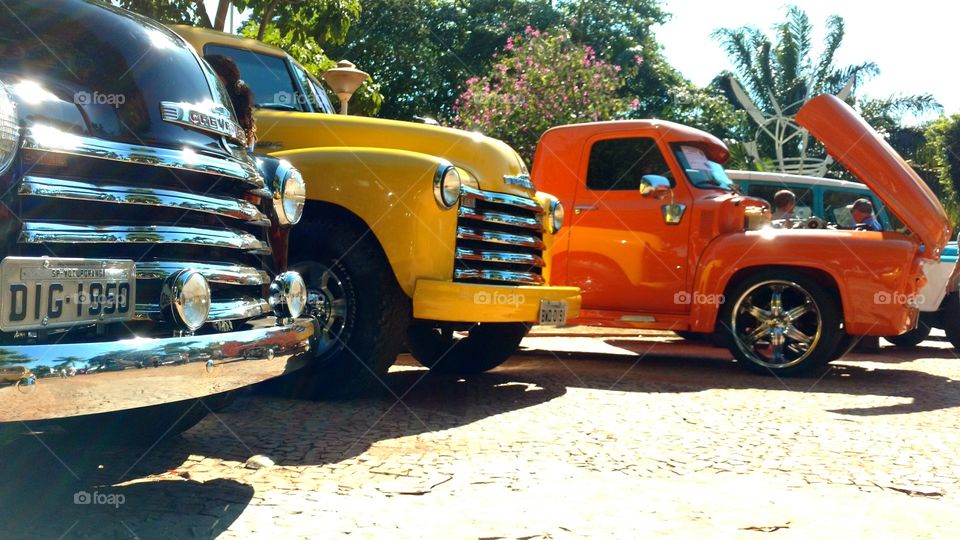 Frentes maravilhosas de camionetes/pick up de cores preta, amarela e  laranja, em evento de colecionadores de automóveis antigos.