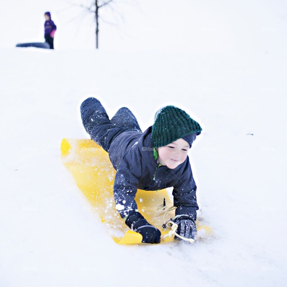 Boy sledding down a hill in winter 