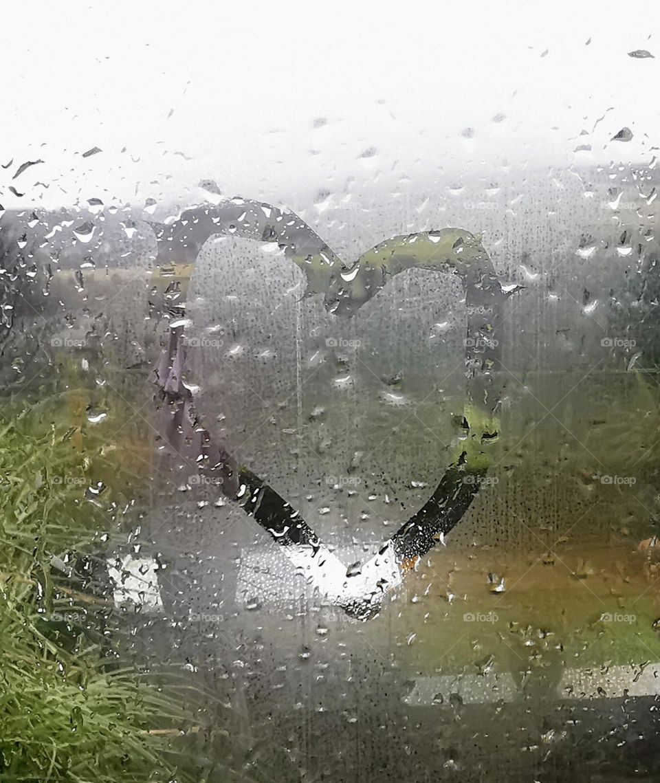 Heart drawn in condensation on window with raindrops behind