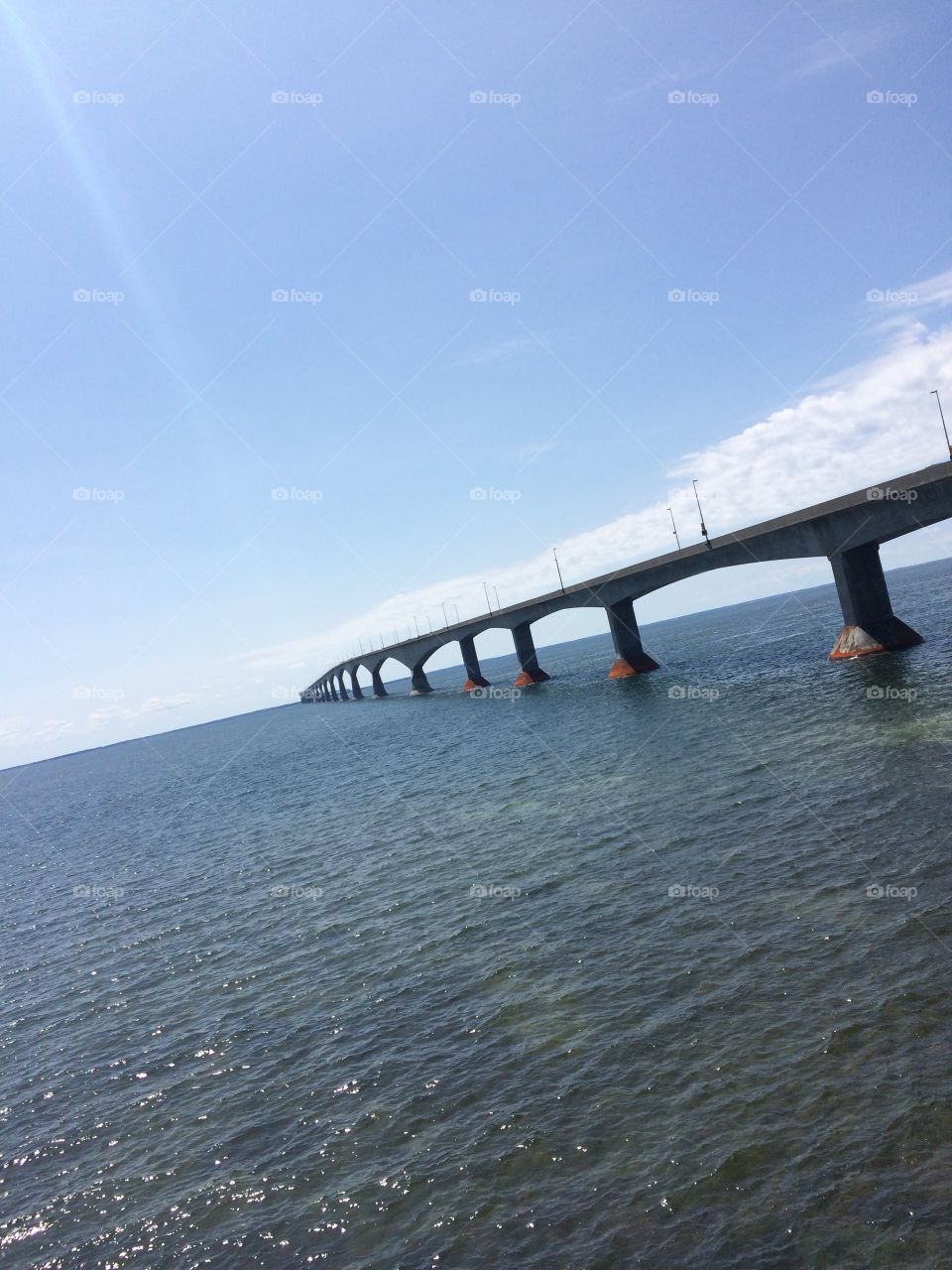 A beautiful photo of the Confederation Bridge taken off the shore of Prince Edward Island with a clear blue sky. 
