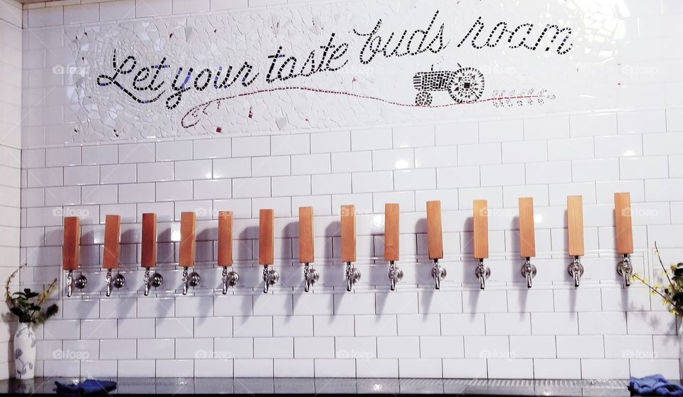 Shabby chic stone white tiled wall filled with rustic wood craft brewed beer taps decorated with country theme elements such as tractor and quote - Free Range Brewing in Noda of Charlotte, NC.