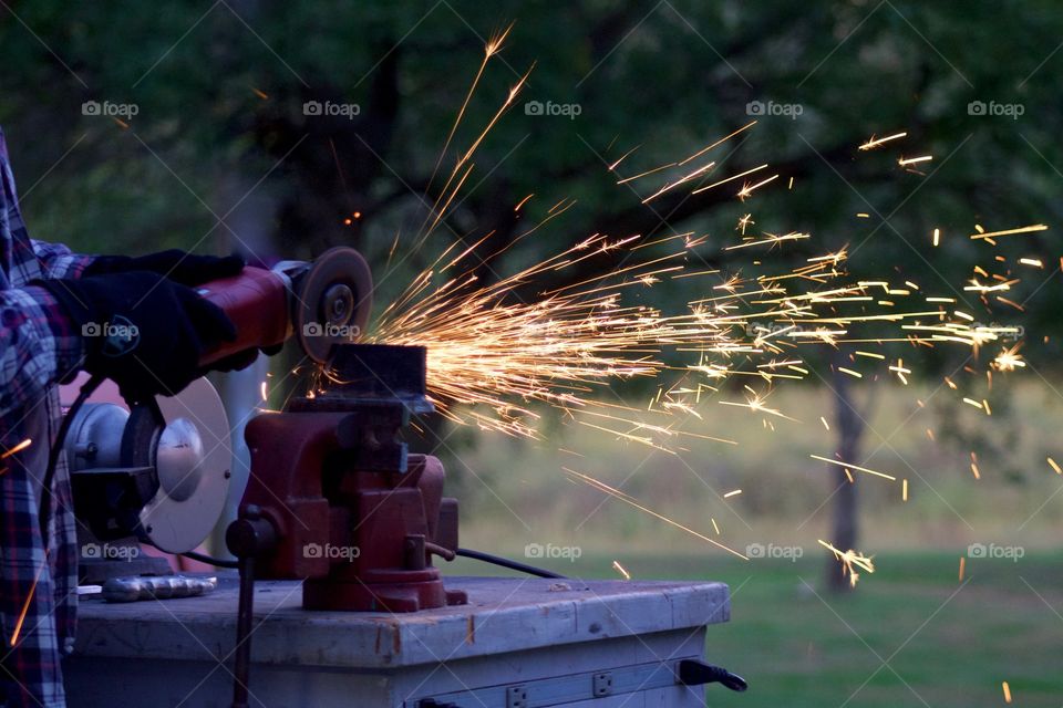 Side view of sparks from a bench grinder being used by a man on a metal part