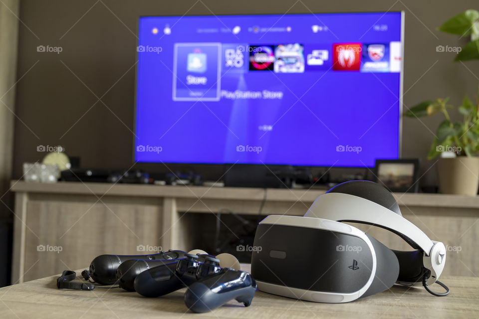 A portrait of everything you need to play a PlayStation vr game. A PlayStation controller, two move controllers and a virtual reality headset in front of a television displaying the PlayStation home screen.