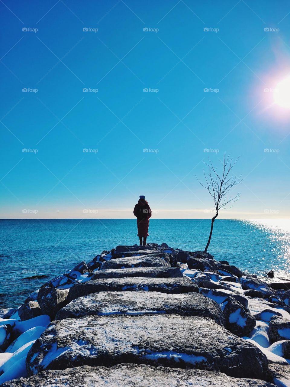 Woman in coat standing at the beach at lake Ontario in winter time.