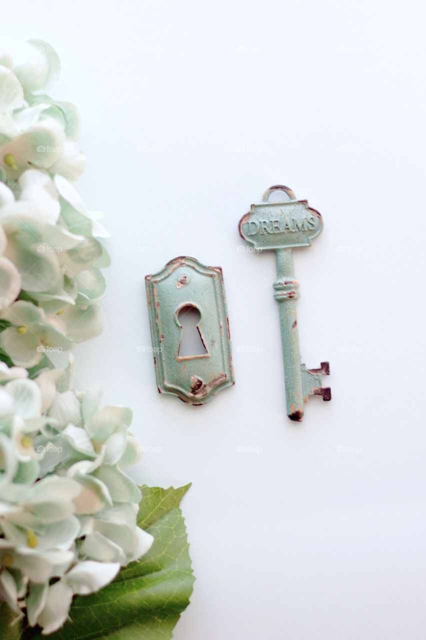 Overhead view of light teal, vintage, metal key with embossed word, “Dreams,” and keyhole with light teal hydrangeas on white background - 