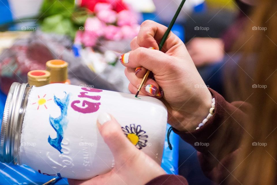 A woman paints a mason jar with colorful objects and symbols during an art class 