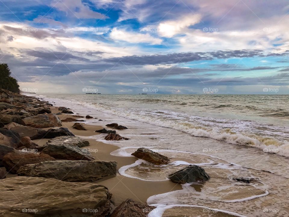 Cloudy sky in the evening above rocky beach licked by foamy tidal waves in southern Thailand