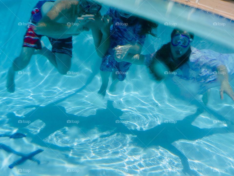 Three persons, dad and two children swimming under the water with their shadows on the bottom of the pool.