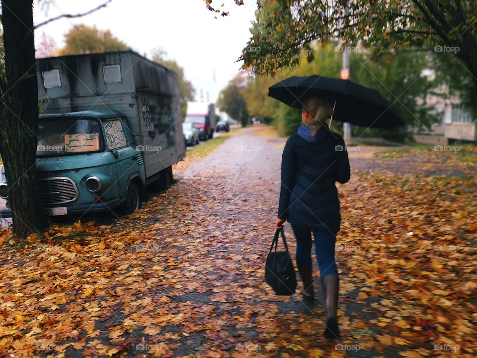 Walking with umbrella by the road with fallen leaves 