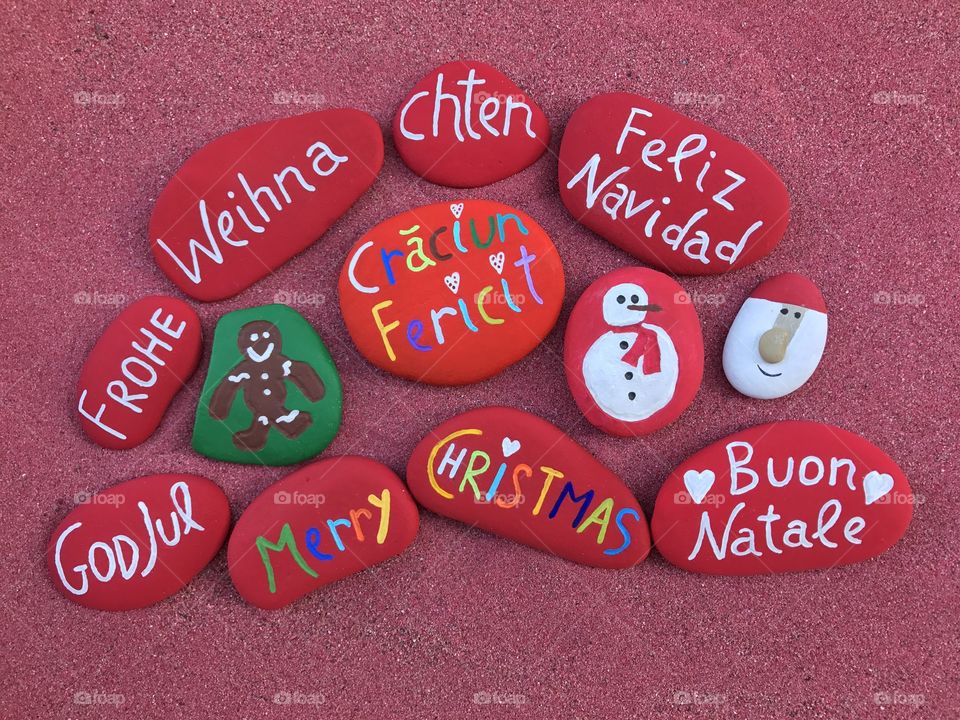 Merry Christmas in many languages with stones design on red sand 