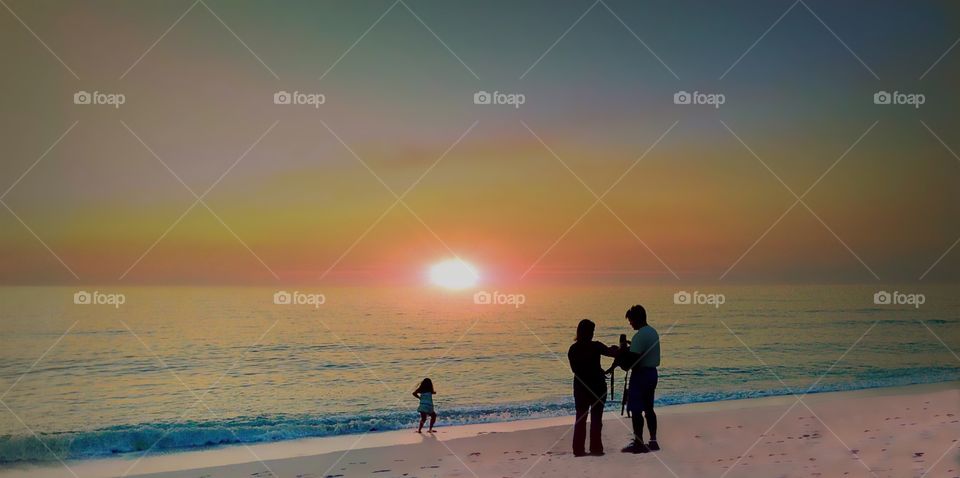 A family enjoying an oceanside sunset full of bold golden and pink colors.