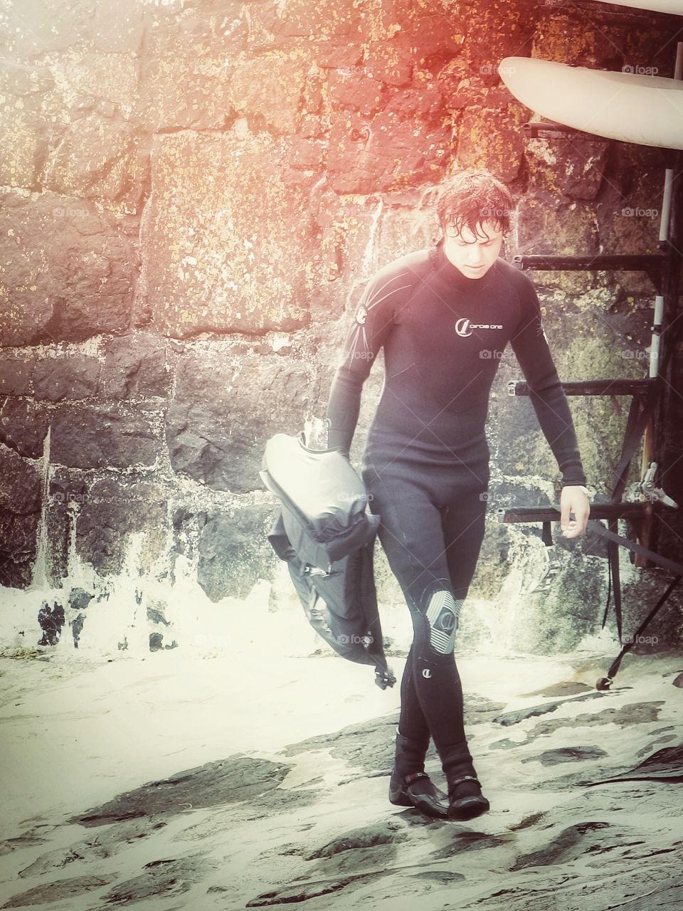 Walking windsurfer. A male windsurfer in a wetsuit walking with his life jacket along a harbour wall.