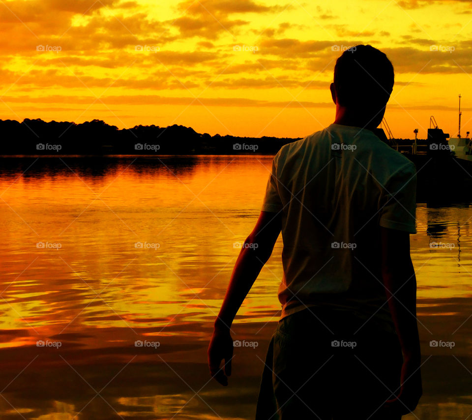 Overseeing a sunset on the bay. A young man oversees a spectacular golden sunset over the Choctawhatchee Bay, in awe!