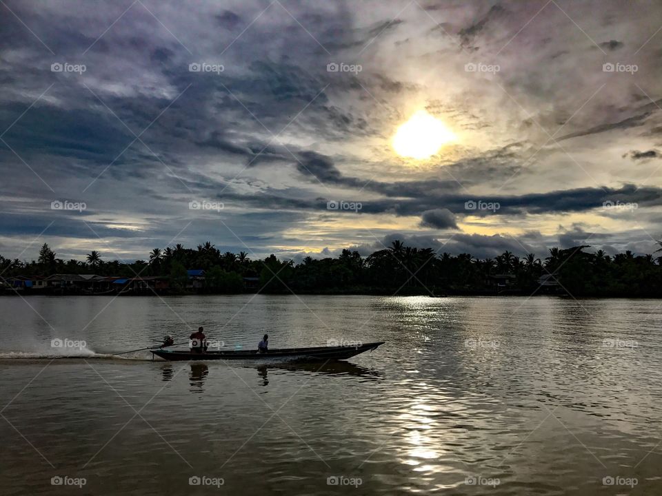 Long-tail fishing boat in the Tapi River under cloudy sunset sky in Surat Thani, southern Thailand