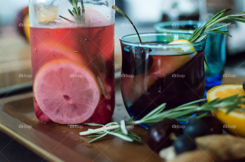 Fresh summer drinks in vintage blue glasses on dark wood serving tray made with ginger root, orange, lemon and raspberry flavored water with cherry, blueberry, mint and rosemary herb fragrant garnish 