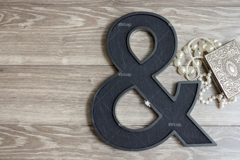 An engagement ring placed inside an ampersand with a vintage jewelry box and pearls 