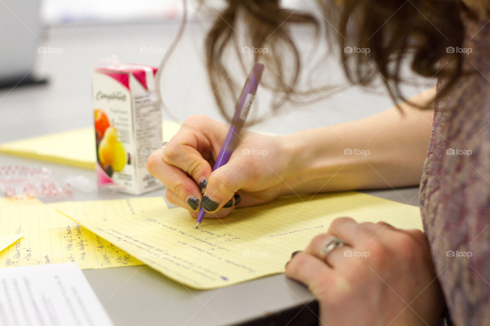 A girl writes notes on yellow paper while in a class