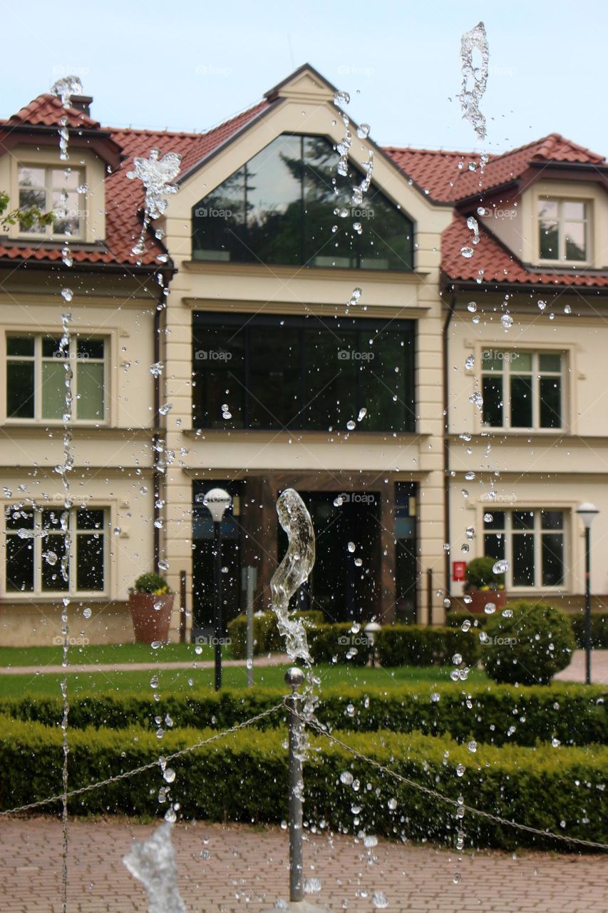 Close Up of Splashes from a Fountain in a City Park against the Backdrop of Buildings on a Warm Spring Day