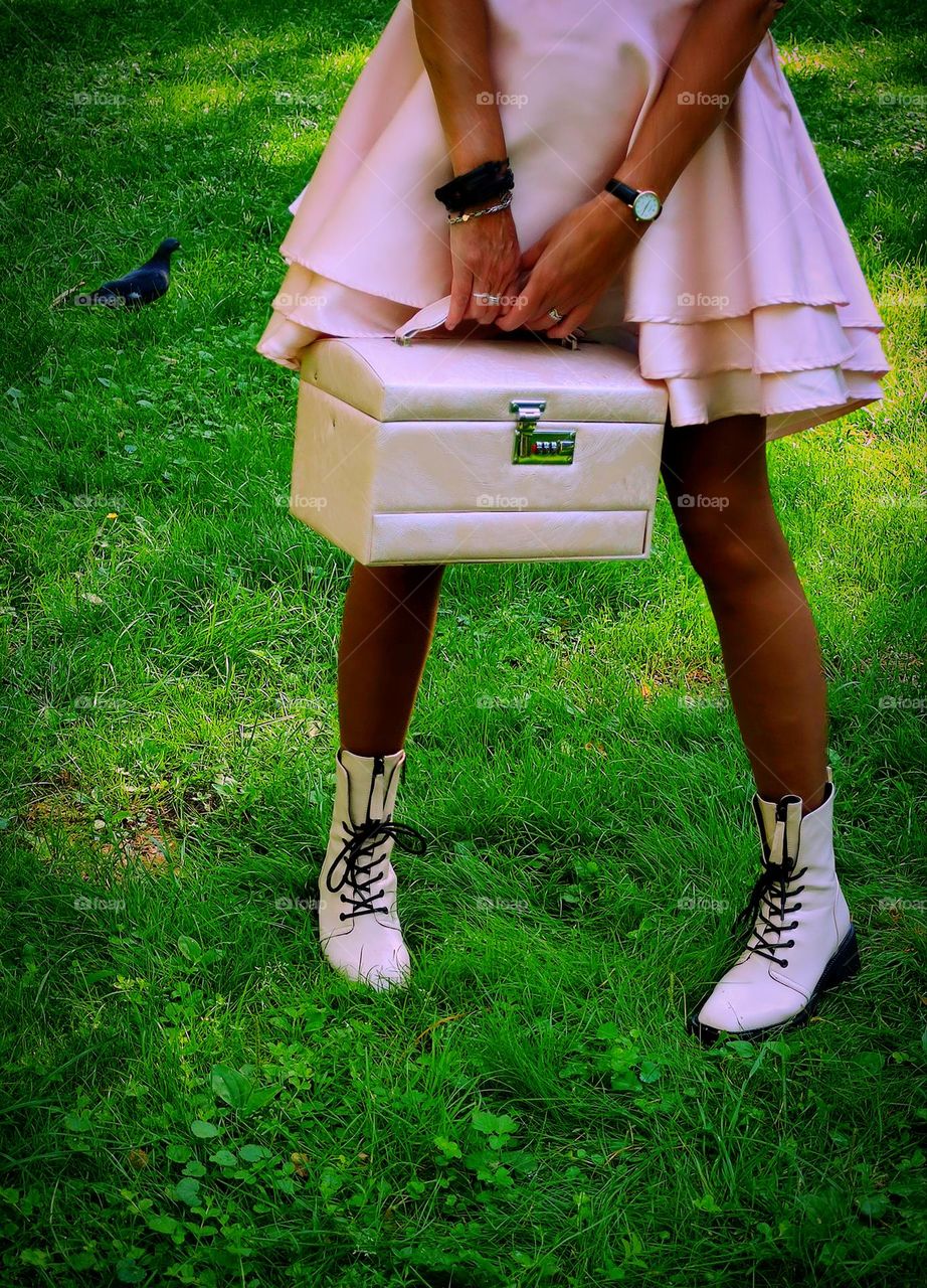 Barbie style.  On the green lawn.  The lower body of a woman: a short pink skirt with flounces.  Hands holding a pink chest