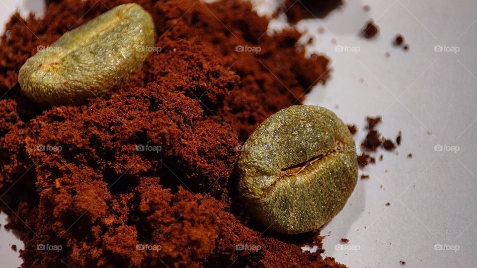 macro image of golden colour Coffee beans above coffee powder on a white surface