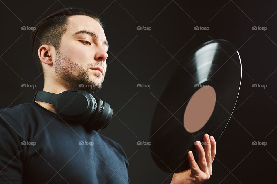 Man looking at vinyl record. Vintage music style. Male with headphones holding old music disk standing on black background. Retro music. Classic audio