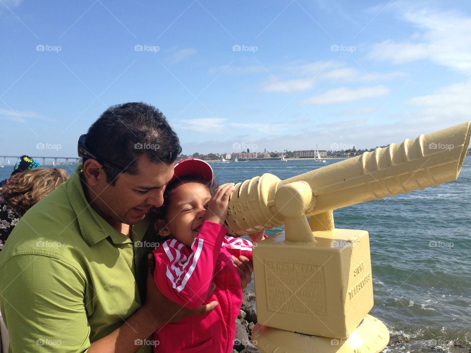 Father and daughter looking with binoculars at sea