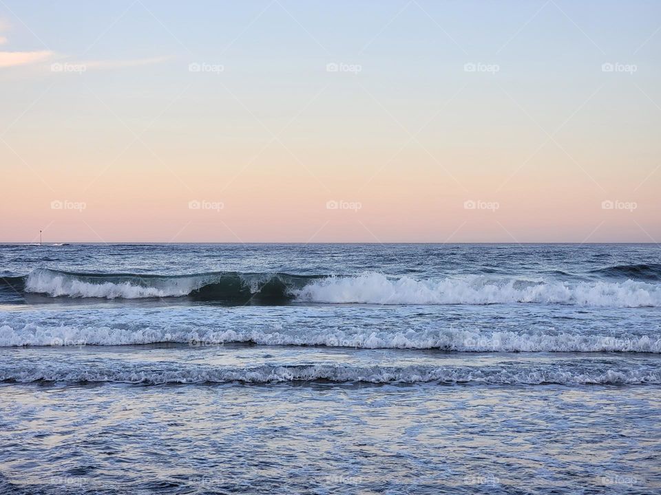 Crashing Waves on an Ocean Shore with a Blue and Pink Pastel Sky in the Horizon