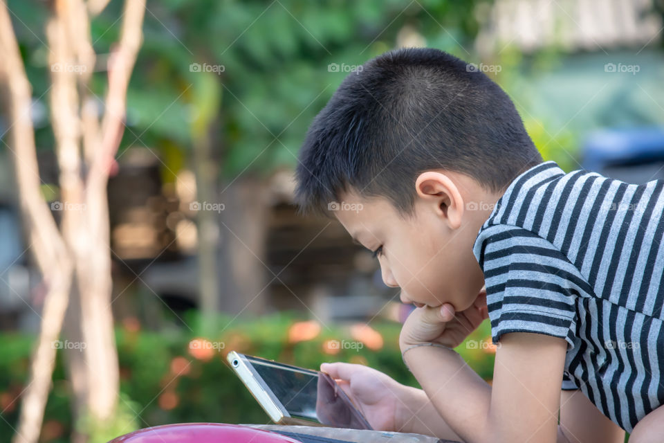 Portrait of Asian boys are playing mobile phones in park.