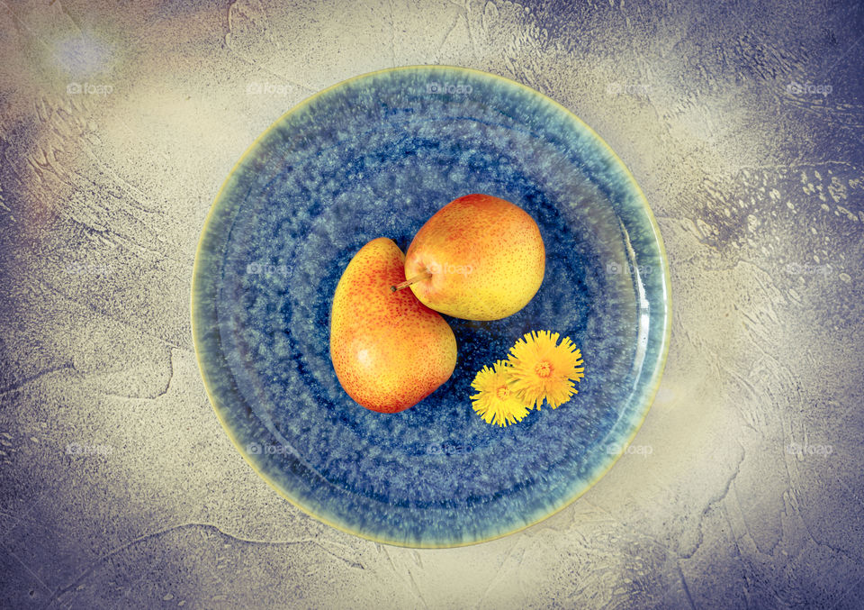 Fresh, ripe, sweet pears with yellow flowers on textural, beautiful plate on blue background. Concept of beauty of natural, seasonal fruits and vegetables. Food photo, horizontal orientation