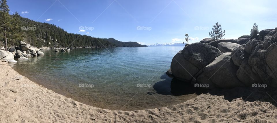 A panoramic view of a secretive corner of a Sierra lake. Warm tones characterize the rippling water upon the shore. 