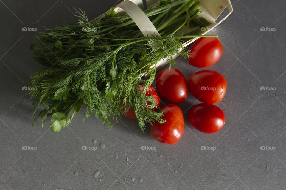 Fresh, bright, juicy vegetables and herbs for preparing salads and other vegetable dishes are on a gray, kitchen worktop.