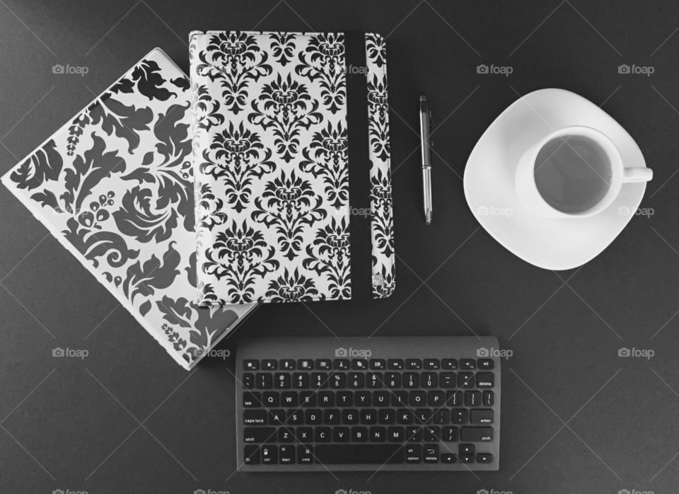 Top view desk - tablet, binder, Bluetooth keyboard, stylus, tea in cup with saucer in black and white